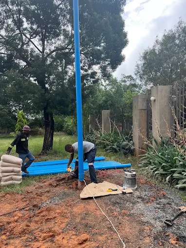 Blue PVC borehole casing being lowered into a freshly drilled hole